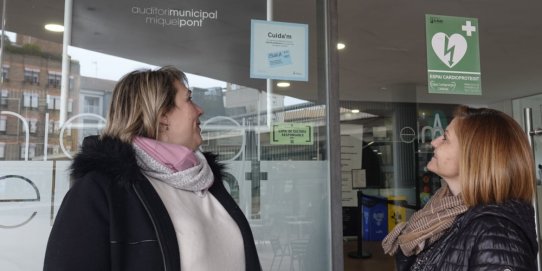 Les regidores de Diversitat Funcional i d'Activitat Econòmica, Anna Margalef i Anna Màrmol, davant l'adhesiu que hi ha a l'entrada de l'Auditori.